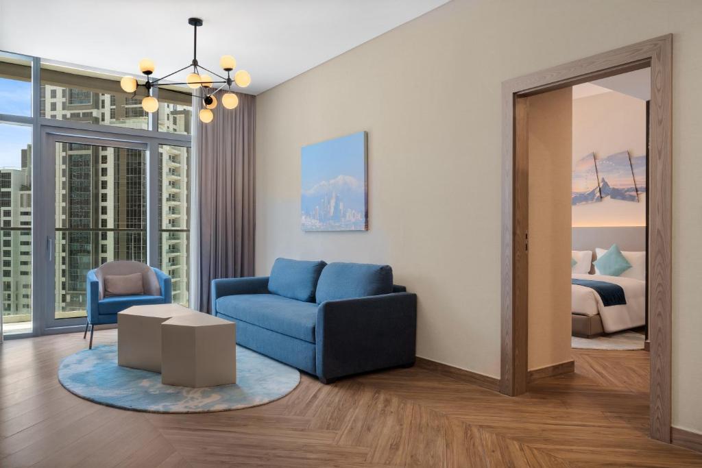 a living room with a blue couch and a bedroom at Paramount Hotel Midtown in Dubai