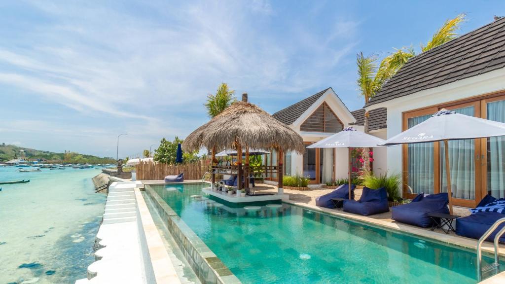 a swimming pool with chairs and umbrellas next to a house at Segara Seaside Resort in Nusa Lembongan