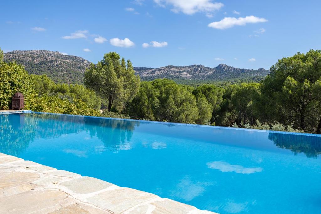 una piscina azul con árboles y montañas en el fondo en Casa De Cuento, en San Martín de Valdeiglesias
