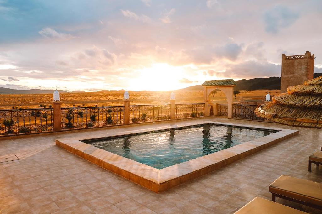 a swimming pool on a balcony with the sunset in the background at Porte De Sahara Ouzina in Ouzina