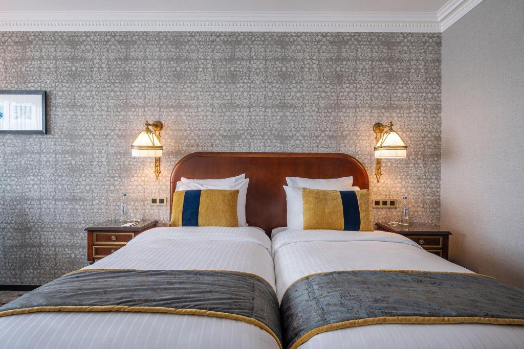 a bedroom with two beds and two lamps on the wall at Hotel Barsey by Warwick in Brussels