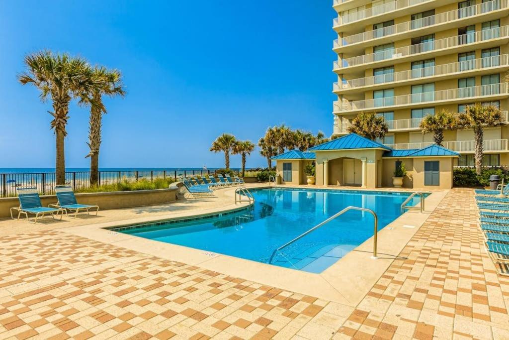 a swimming pool with palm trees and a building at Bluewater Vacation Rentals in Orange Beach