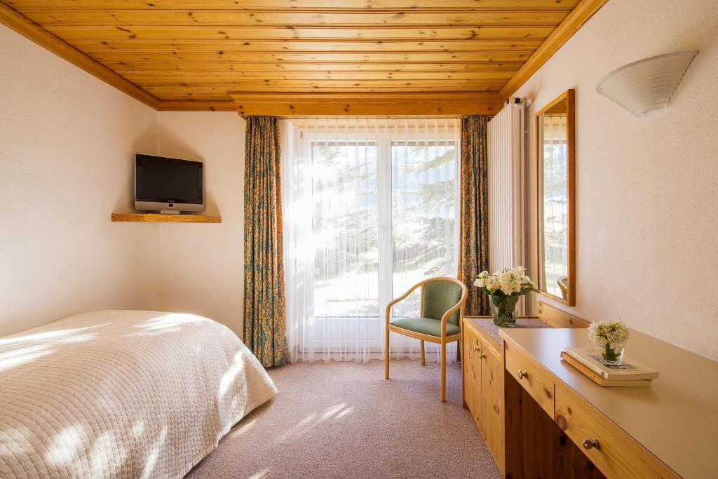 a bedroom with a bed, chair, desk and a tv at Hotel Europa St. Moritz in St. Moritz