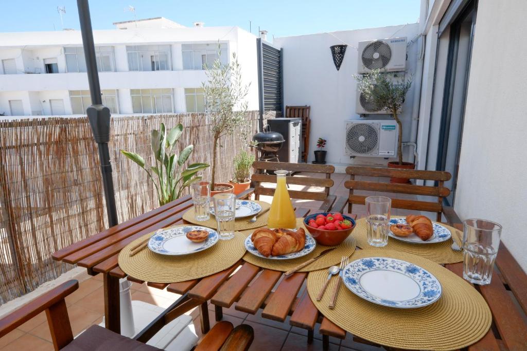 a wooden table with plates of food on a balcony at Spacious terrace, swimming pool, private parking in Olhão