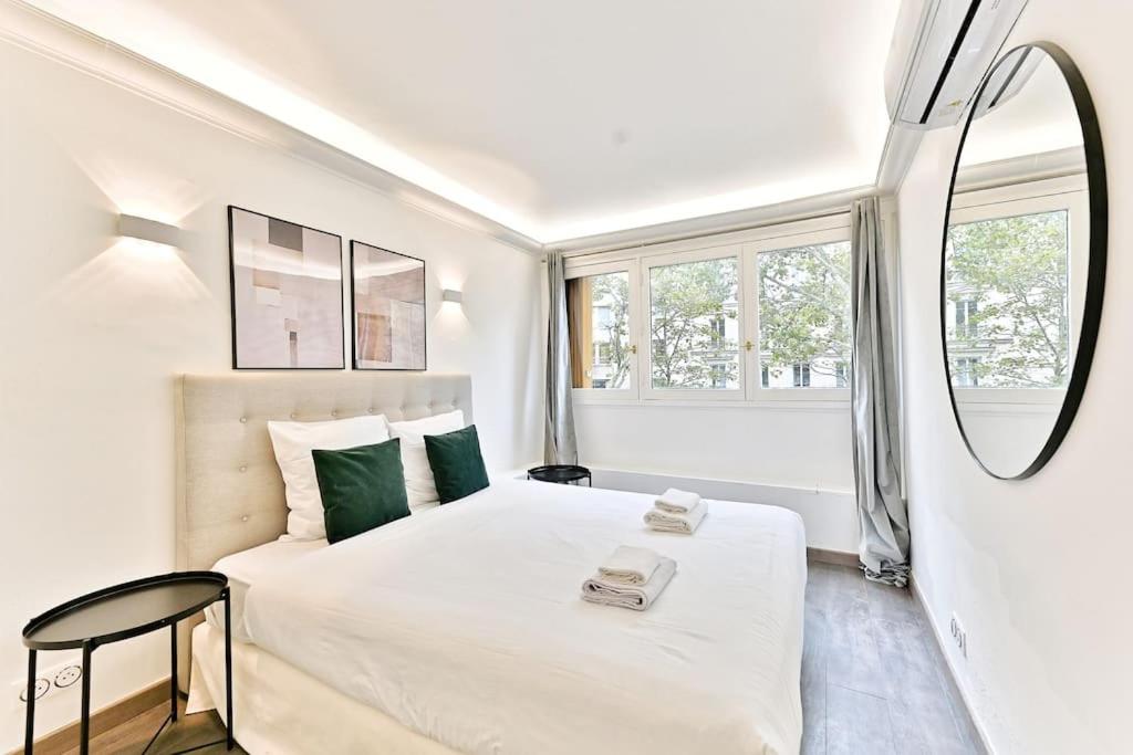 une chambre blanche avec un lit et un miroir dans l'établissement Appartement ensoleillé proche Buttes Chaumont, à Paris