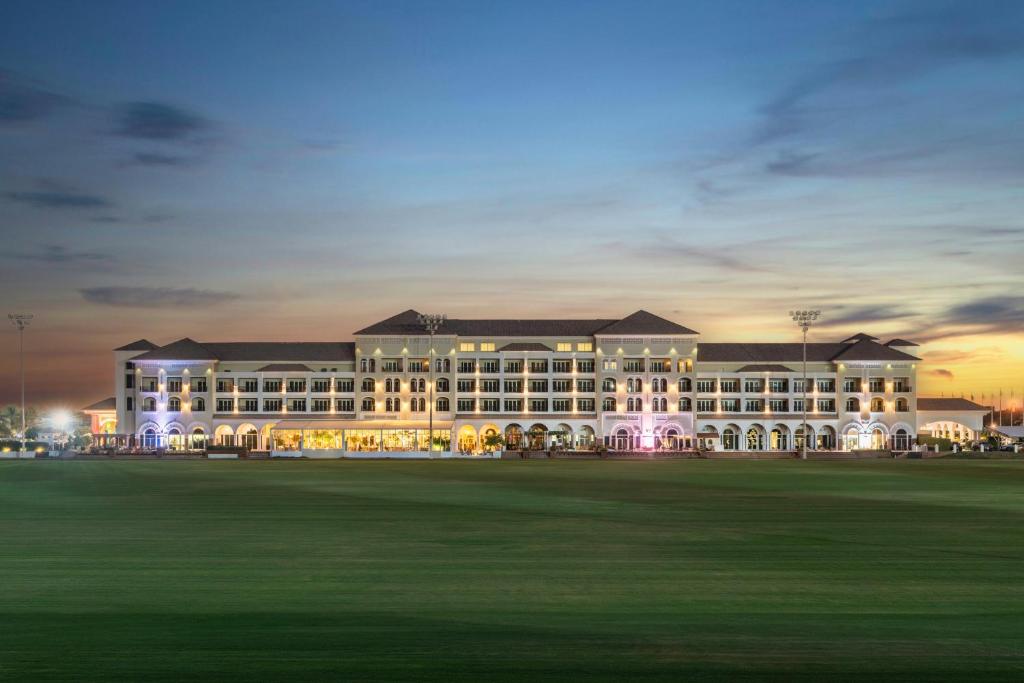 un grand bâtiment avec un champ vert devant lui dans l'établissement Al Habtoor Polo Resort, à Dubaï