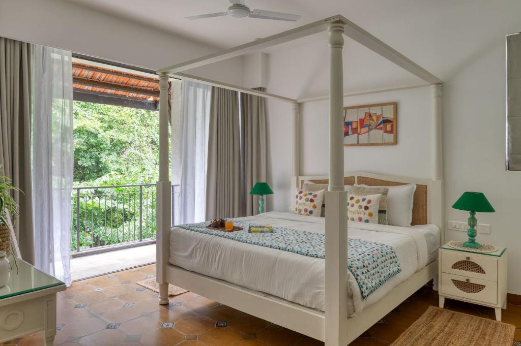 a bedroom with a canopy bed and a balcony at Radiant 1BHK Apartment by tisyastays in Candolim
