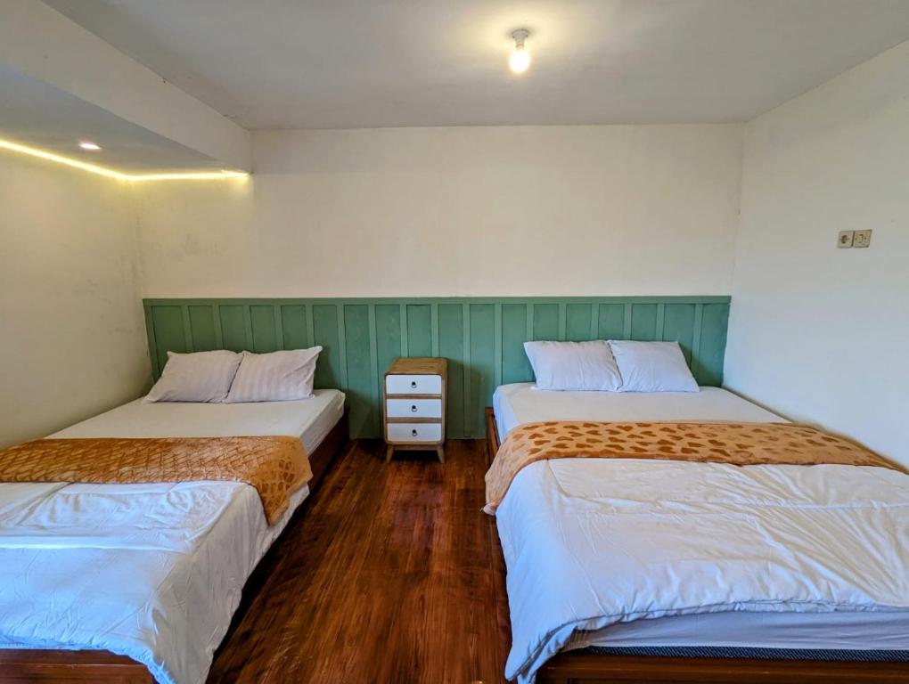 two beds in a room with wooden floors at Homestay Talago minang dieng in Dieng