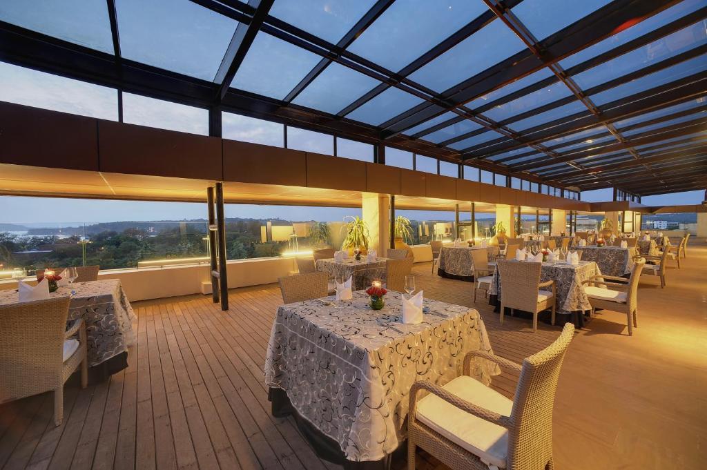 a restaurant with white tables and chairs and windows at Vivanta Goa, Panaji in Panaji