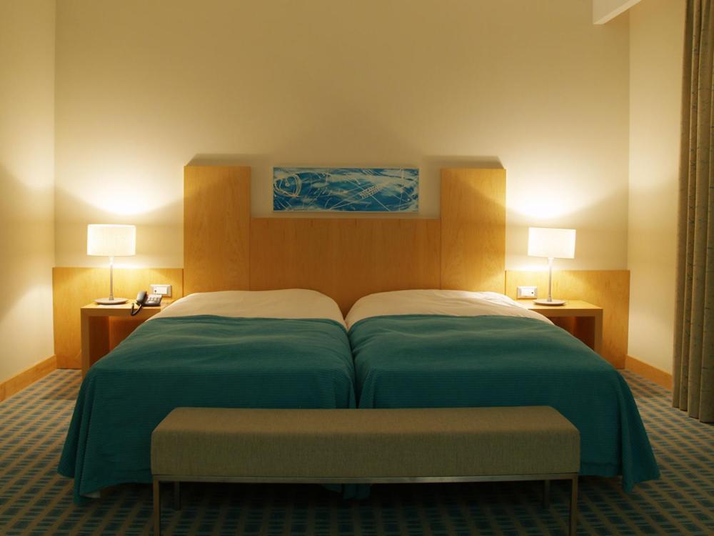 a bedroom with a bed with green sheets and two lamps at Hotel Praia in Nazaré