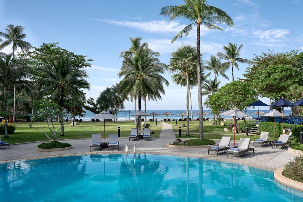 a pool with chairs and palm trees and the ocean at Phuket Marriott Resort & Spa, Merlin Beach in Patong Beach
