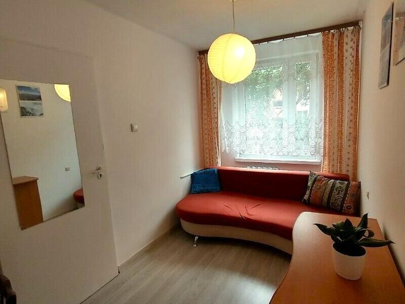 a living room with a red couch in front of a window at Słoneczny Pokój w bloku na 1 p dla 1 Niepalącej Osoby od 1 do 12 miesięcy in Kraków