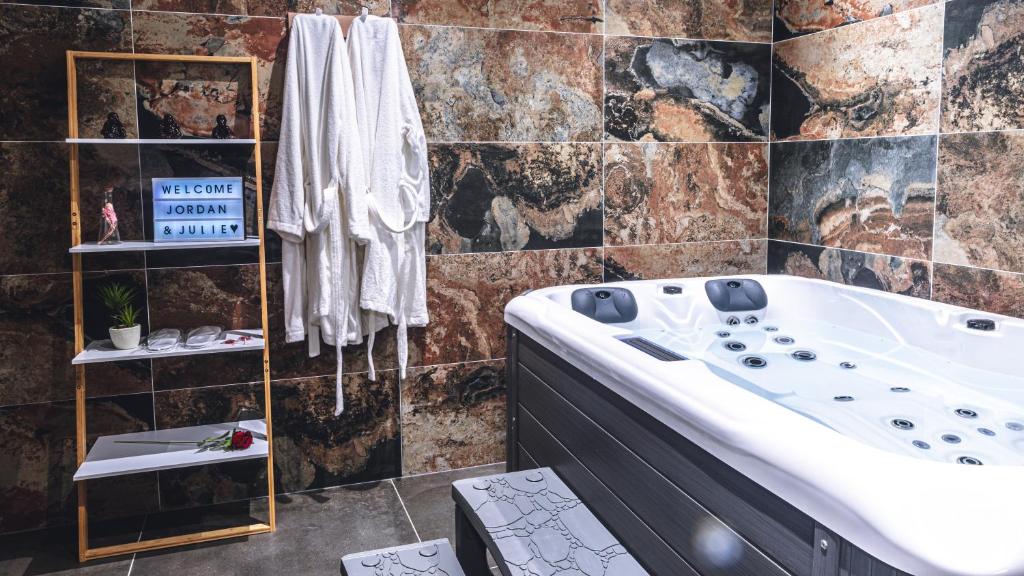 La salle de bains est pourvue d'une grande baignoire et d'un mur en carrelage. dans l'établissement Évasion room spa, à Hénin-Beaumont