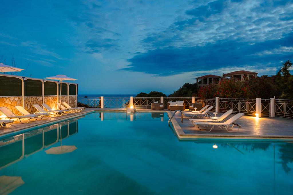 a pool with lounge chairs and the ocean at night at Costa Avithos in Svoronata