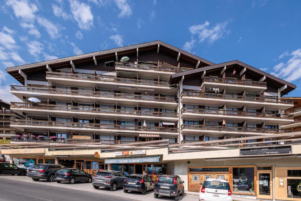 Un gran edificio con coches aparcados delante. en Valaisia 17B - 4 pers - centre station, en Nendaz