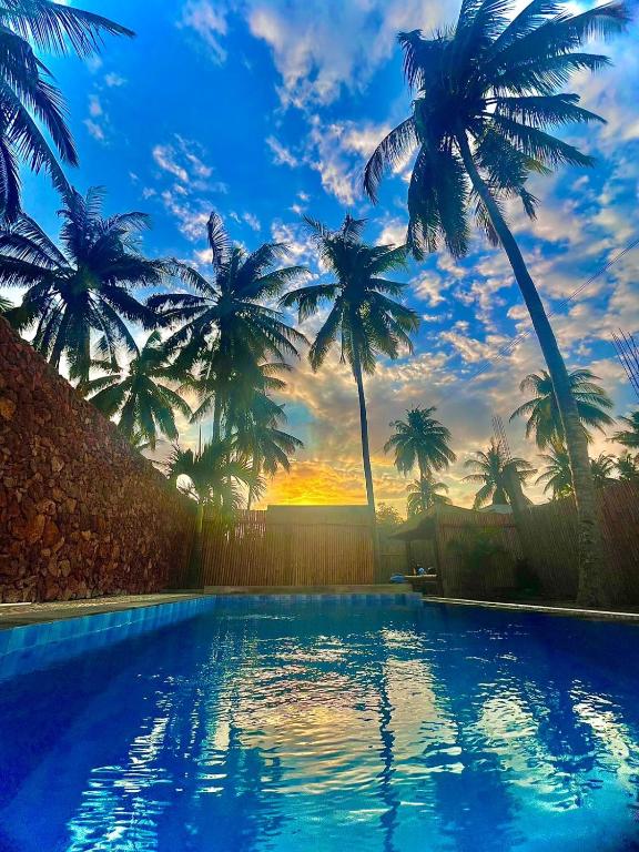 una piscina con palme sullo sfondo di Tata Surf Hostel a Kuta Lombok