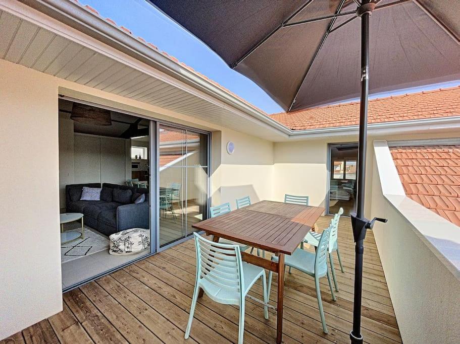 une table et des chaises en bois sur une terrasse avec un parasol dans l'établissement Agréable 3 chambres extra centre à 200m de l'océan, à Biscarrosse