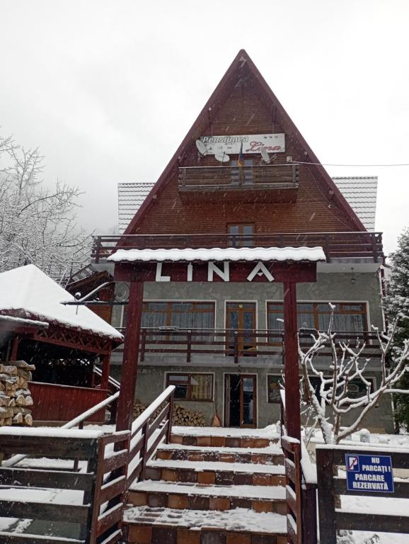 a building with a sign on it in the snow at Pensiunea Lina in Lepşa