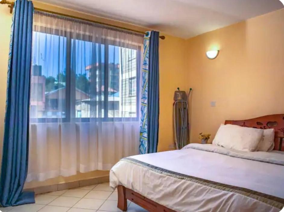 a bedroom with a bed and a large window at Lux Suites Makao Rossyln Apartments in Nairobi