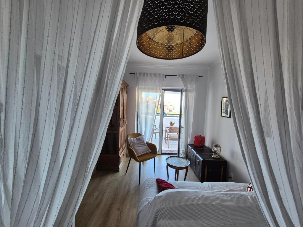 a bedroom with white curtains and a bed and a chair at Villa Alegria in Ericeira