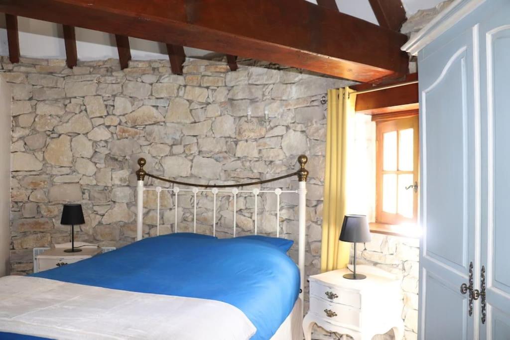 a bedroom with a blue bed and a stone wall at La tour du Périgord in Beaupouyet