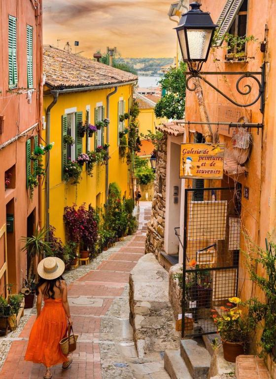 a woman in a hat walking down a narrow street at Hôtel Gabriel in Menton
