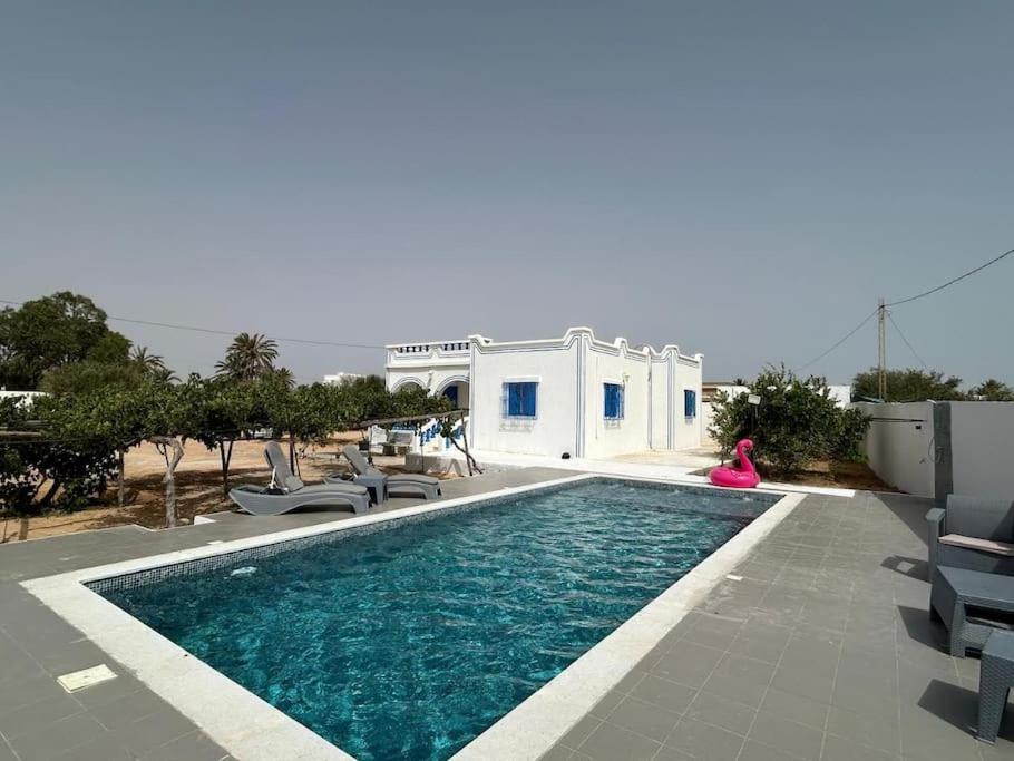 a woman is sitting next to a swimming pool at Villa Djerba Arkou in Djerba