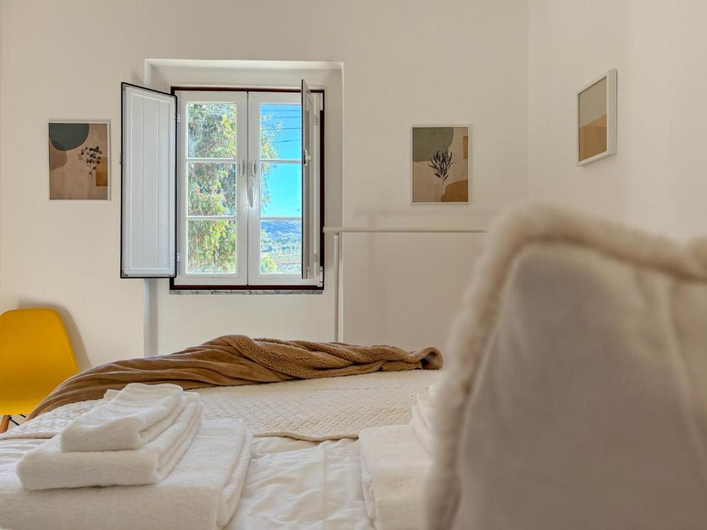 a white bedroom with a bed and a window at Casinha da Serra in Vilar