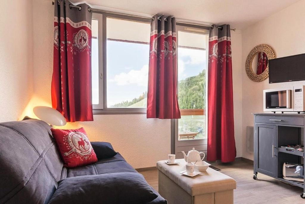 - un salon avec des rideaux rouges et un canapé dans l'établissement Résidence Boedette A - Appartement rénové · Départ et retour skis aux pieds · Balcon vue montagnes MAE-1114, aux Menuires