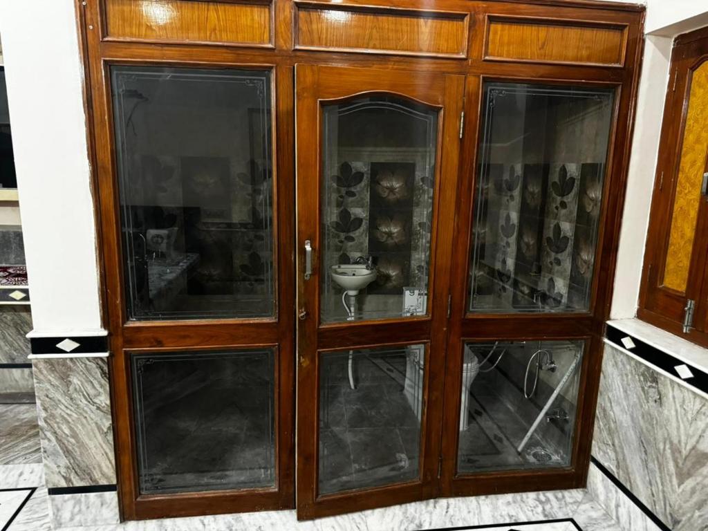 a wooden cabinet with glass doors in a room at Rose Merry Guesthouse in Bikaner