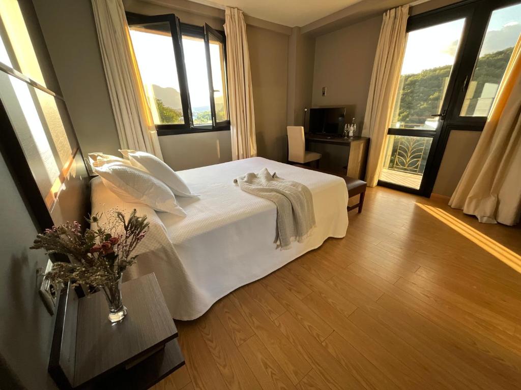 a bedroom with a bed with white sheets and windows at Hotel Don Pablo in Villasana de Mena