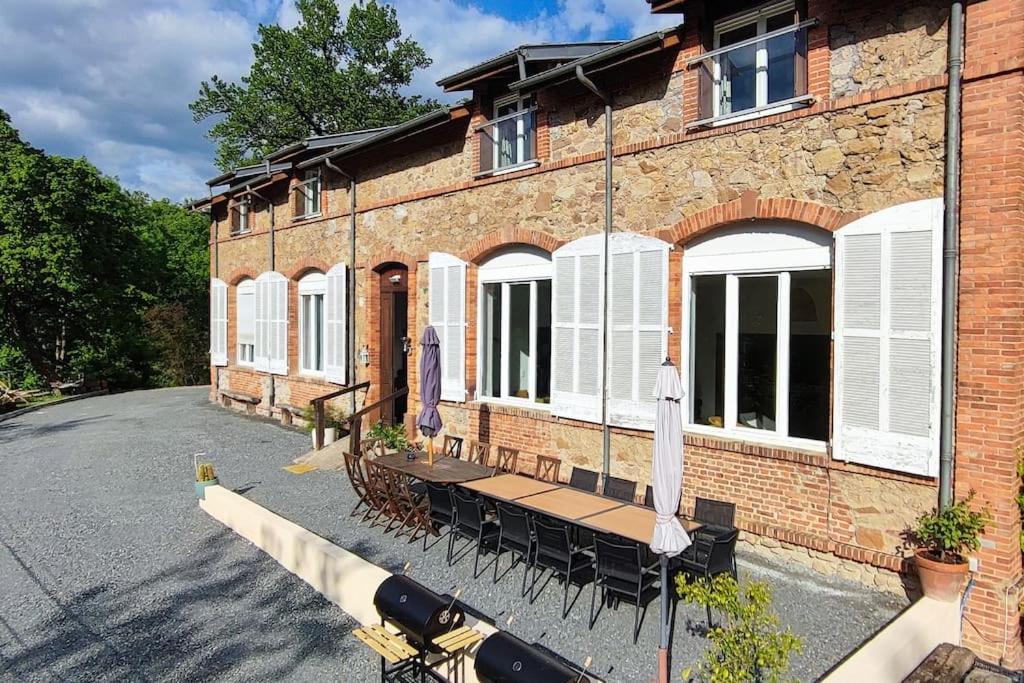 un bâtiment en briques avec des tables et des chaises devant lui dans l'établissement Grande maison familiale la bastide du puech, à Cransac