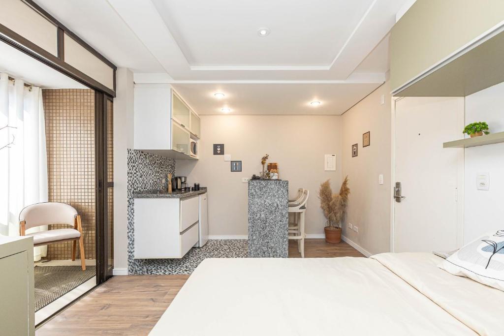 Un dormitorio con una cama blanca y una cocina. en Seu lar no coração de Curitiba, en Curitiba