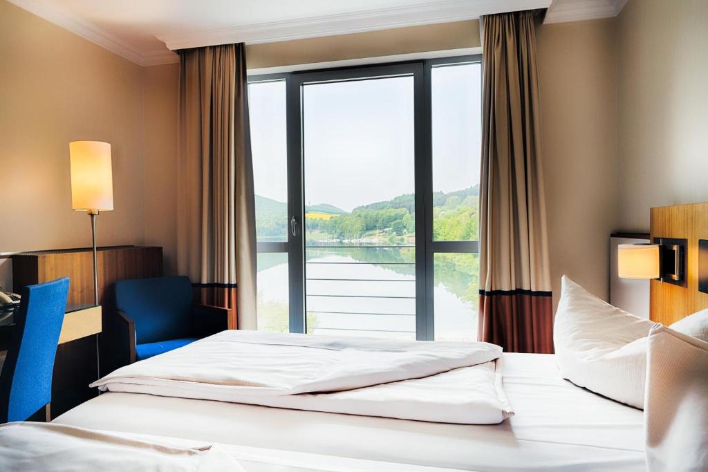ein Hotelzimmer mit zwei Betten und einem großen Fenster in der Unterkunft Welcome Hotel Meschede Hennesee in Meschede