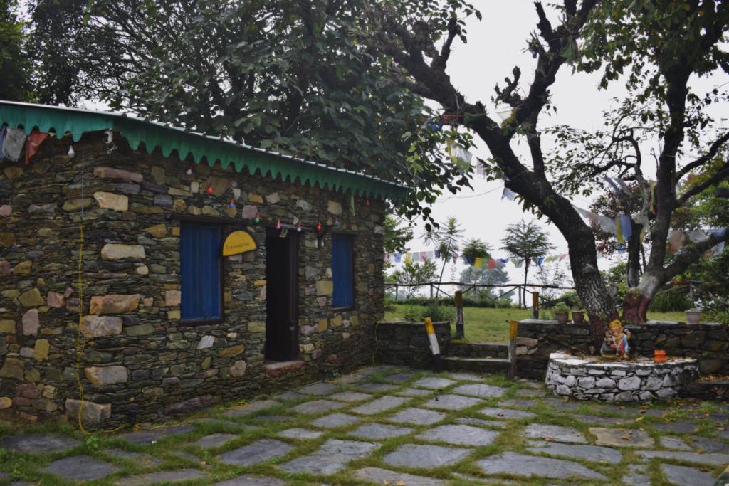 a stone building with blue windows and a tree at Hostel Hideout in Bhīm Tāl