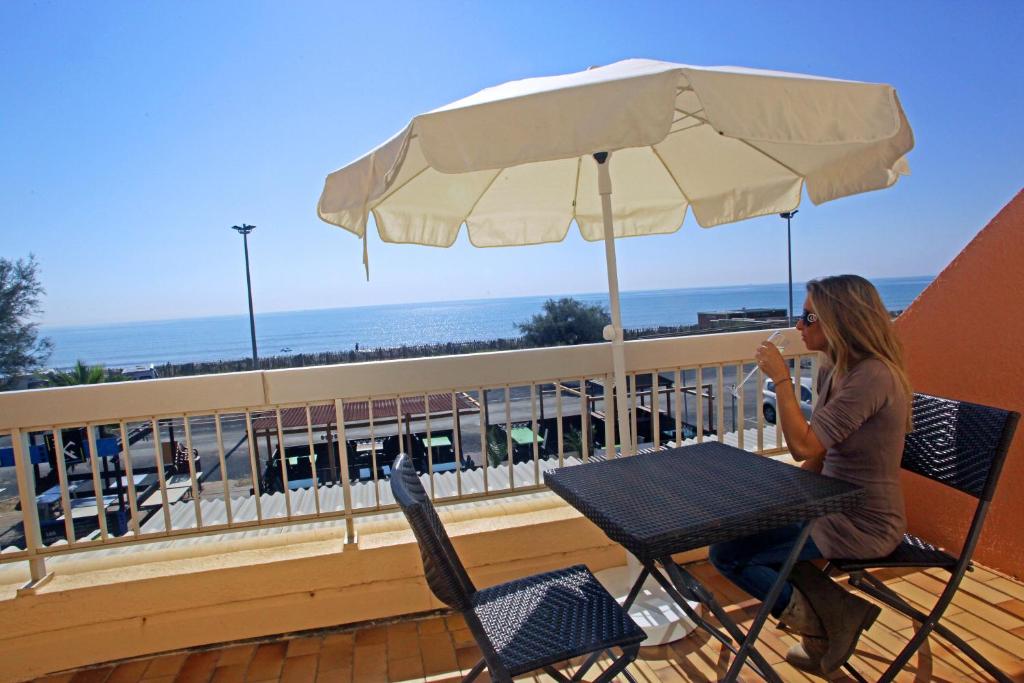 a woman sitting at a table under an umbrella on a balcony at Logis Hotel le Mirador in Portiragnes
