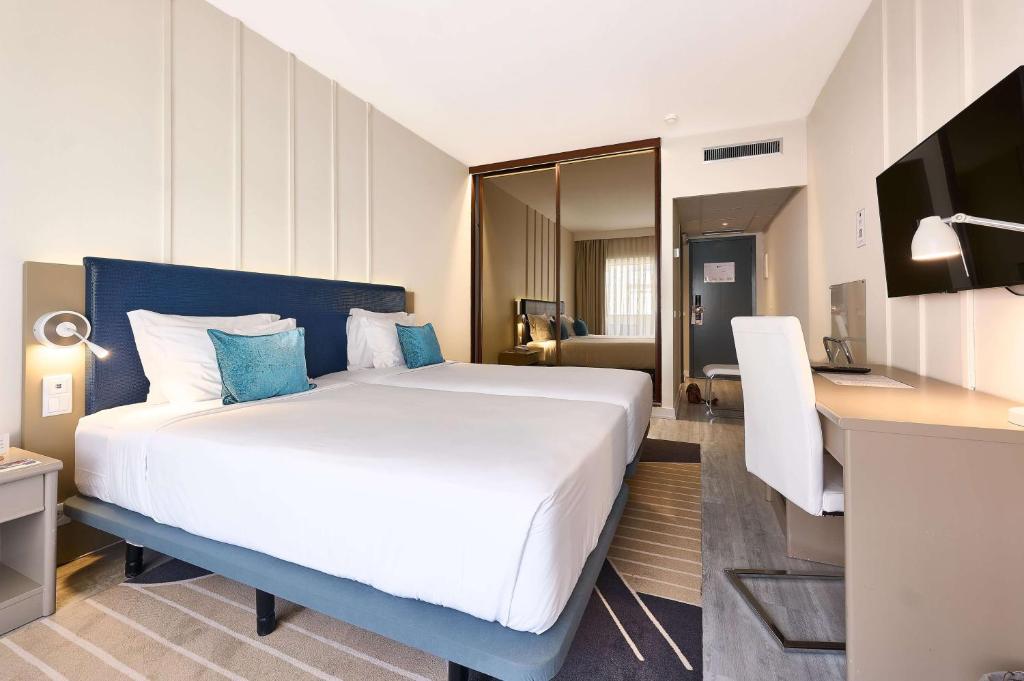 a bedroom with a large white bed and a desk at TRYP by Wyndham Lisboa Caparica Mar in Costa da Caparica