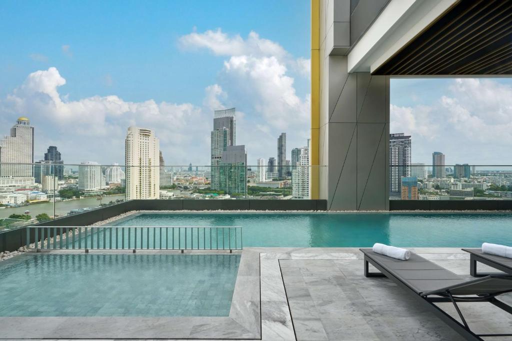 The rooftop pool is pictured against a wide Bangkok skyline with loungers on the tiled deck.