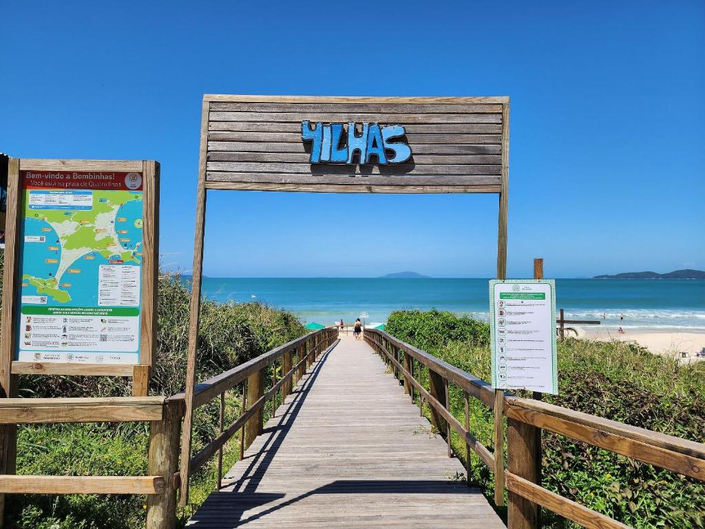 ein Holzsteg zum Strand mit einem Schild in der Unterkunft Acrópole Residence in Bombinhas