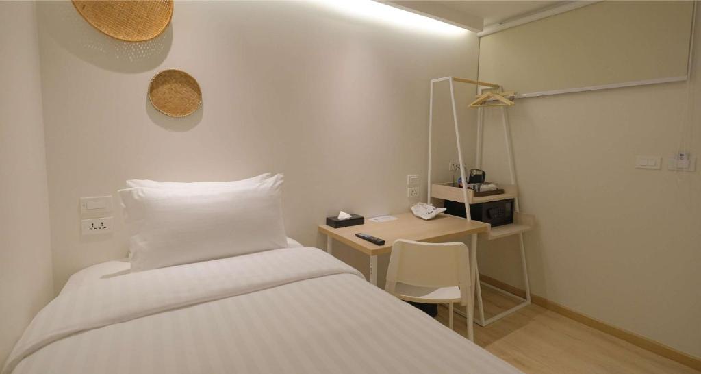A compact single room with a bed, desk, open clothing rail, and minibar area.
