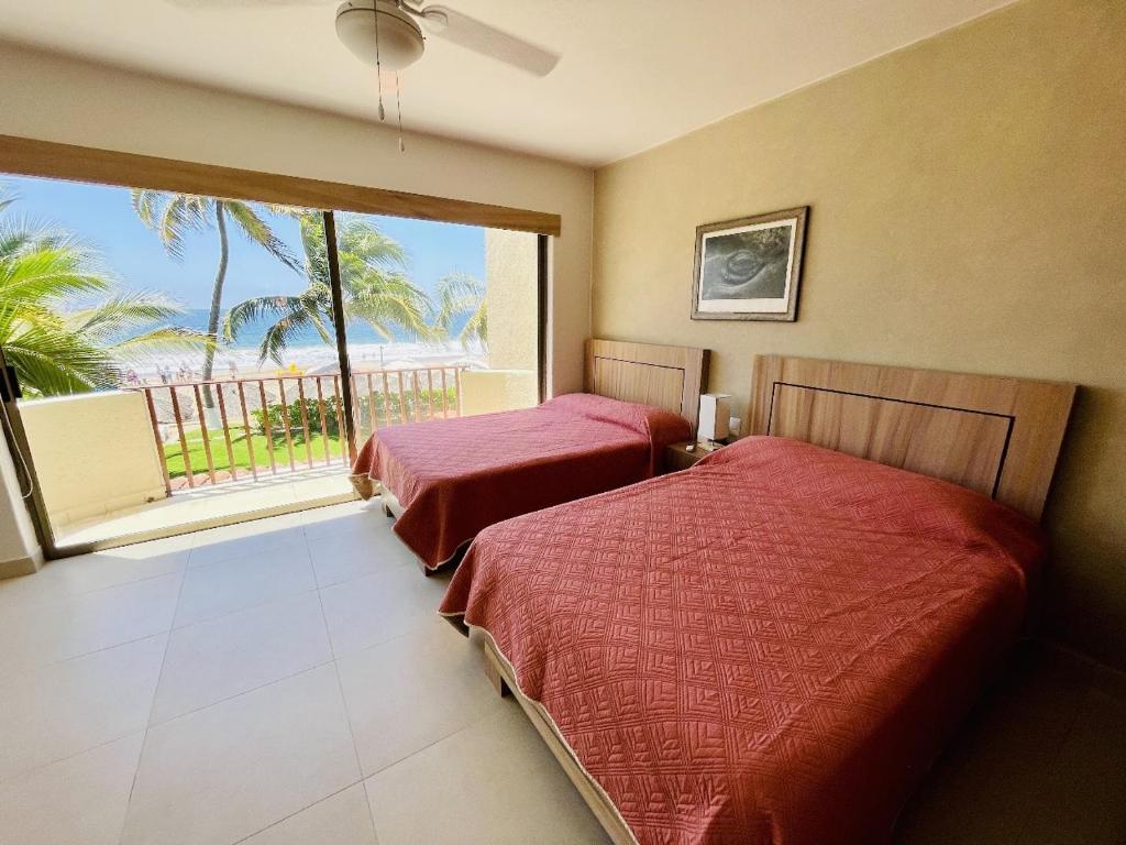 deux lits dans une chambre avec une grande fenêtre dans l'établissement Villa 8 frente al mar, à Zihuatanejo