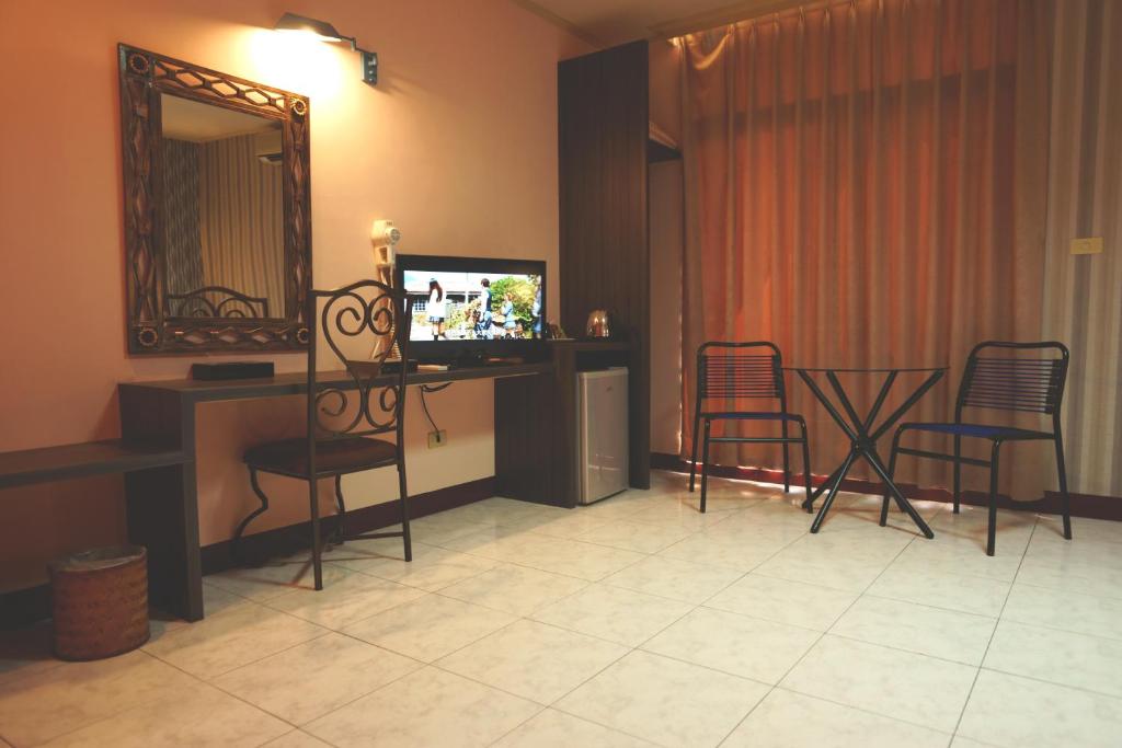 a living room with a desk with a television and chairs at Jiuning Business Hotel in Tainan