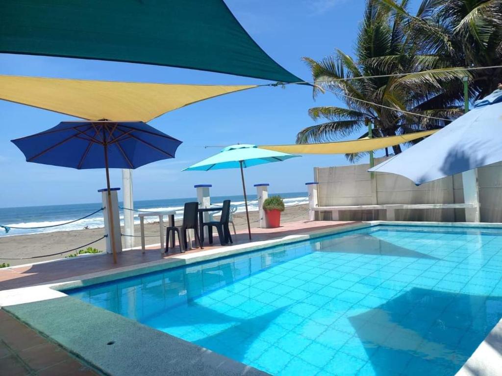 ein Pool mit Sonnenschirmen und Stühlen sowie der Strand in der Unterkunft MARDEORO BEACH HOUSE in Barra de Santiago