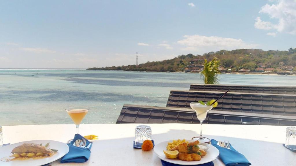 a table with plates of food and drinks and the ocean at Segara Seaside Resort in Nusa Lembongan