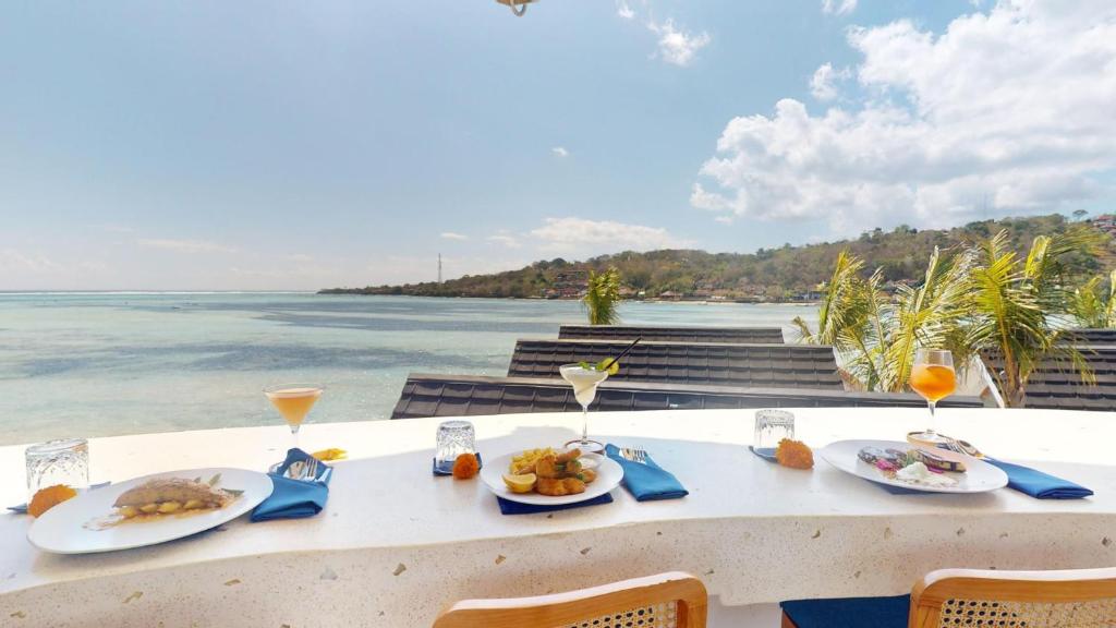 a table with plates of food and the ocean at Segara Seaside Resort in Nusa Lembongan
