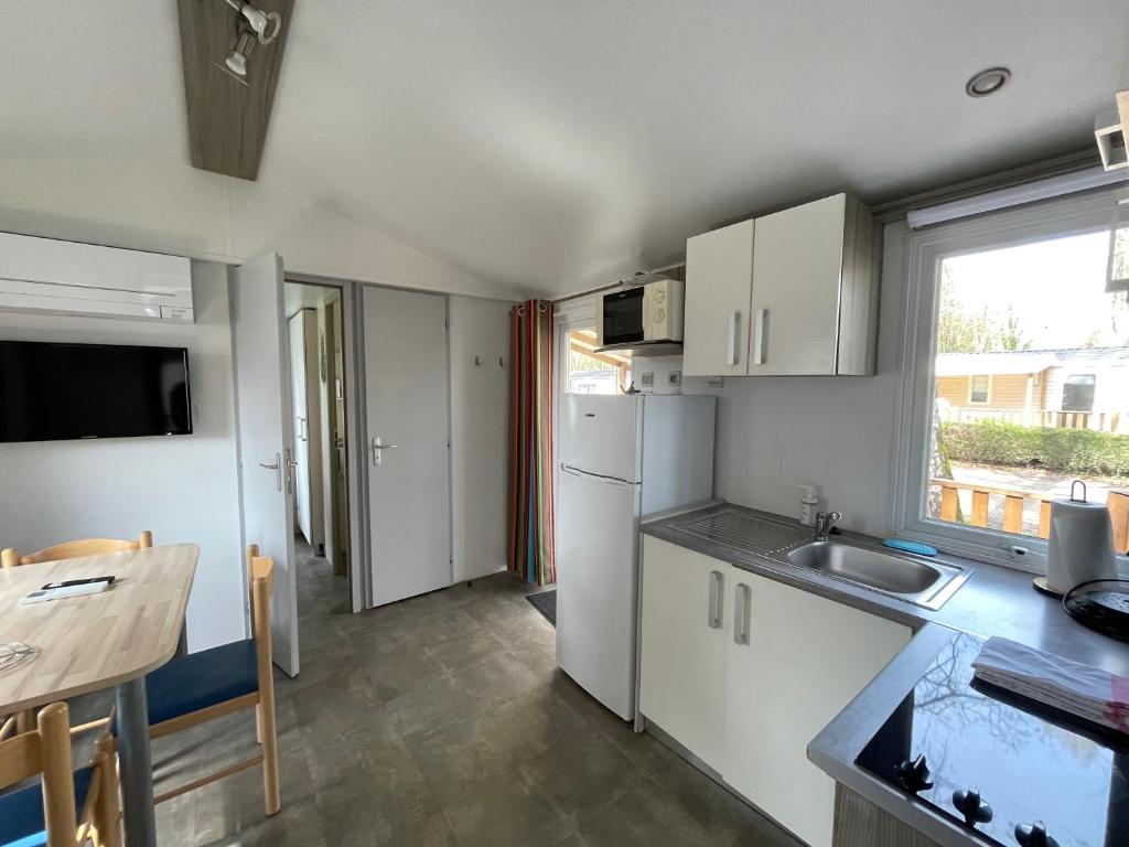a kitchen with white cabinets and a sink and a table at Mobil home Le Riesling 6 personnes climatisé in Boofzheim