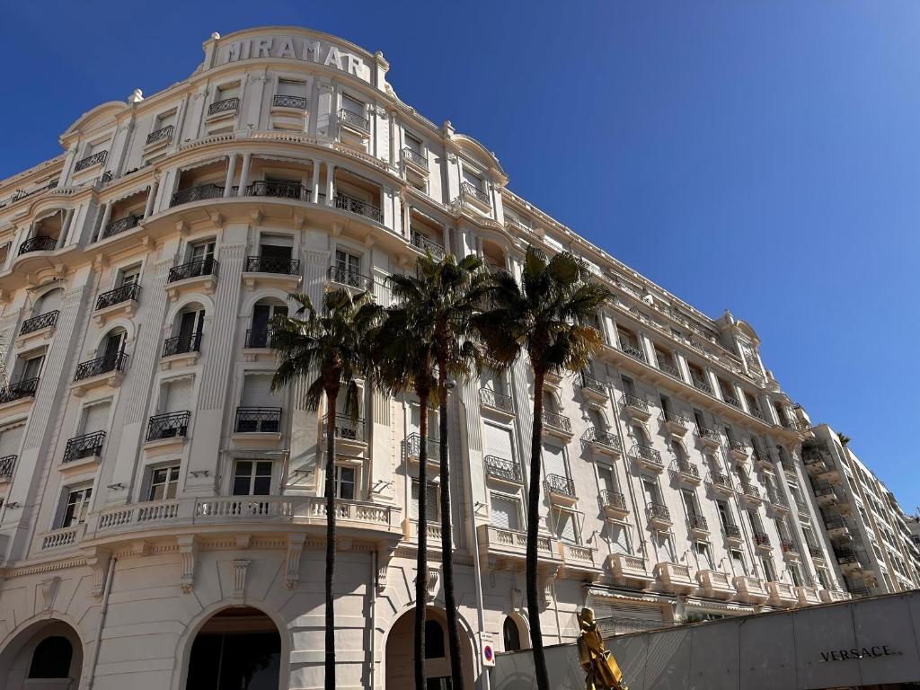 un grand bâtiment blanc avec des palmiers devant dans l'établissement Residence Palais Miramar, à Cannes