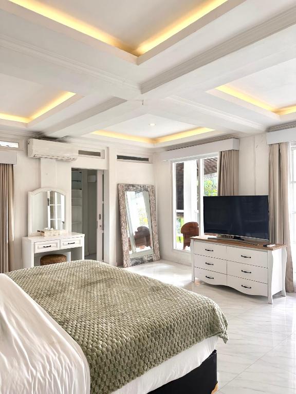 a white bedroom with a large bed and a flat screen tv at Greenhouse Villa in Kerobokan