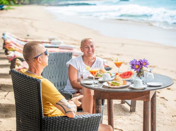 a man and woman sitting at a table on the beach at Frangipani Beach Villa in Tangalle