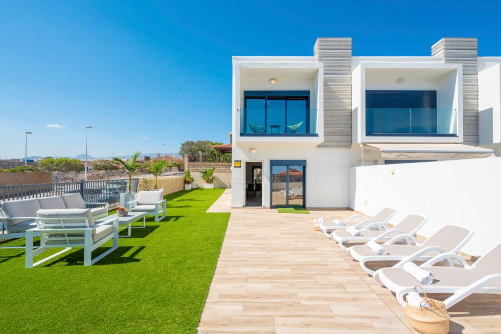 Una fila de sillones blancos en un césped frente a una casa. en MEDANO4YOU La Terraza del Sol, en El Médano